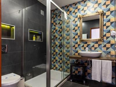 Modern bathroom with colorful geometric wall tiles, glass shower, and sink with towels.
