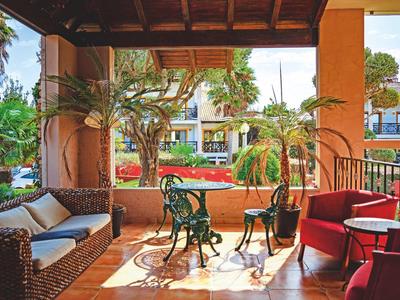 Covered terrace with cozy seating and a view of a garden with flowers and trees.