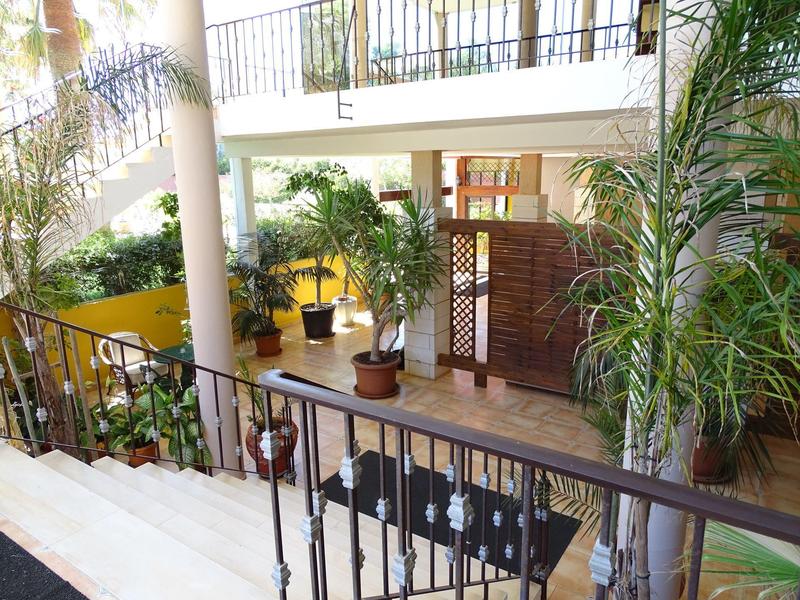 A bright indoor area with stairs, plants, and a table with chairs by a railing.