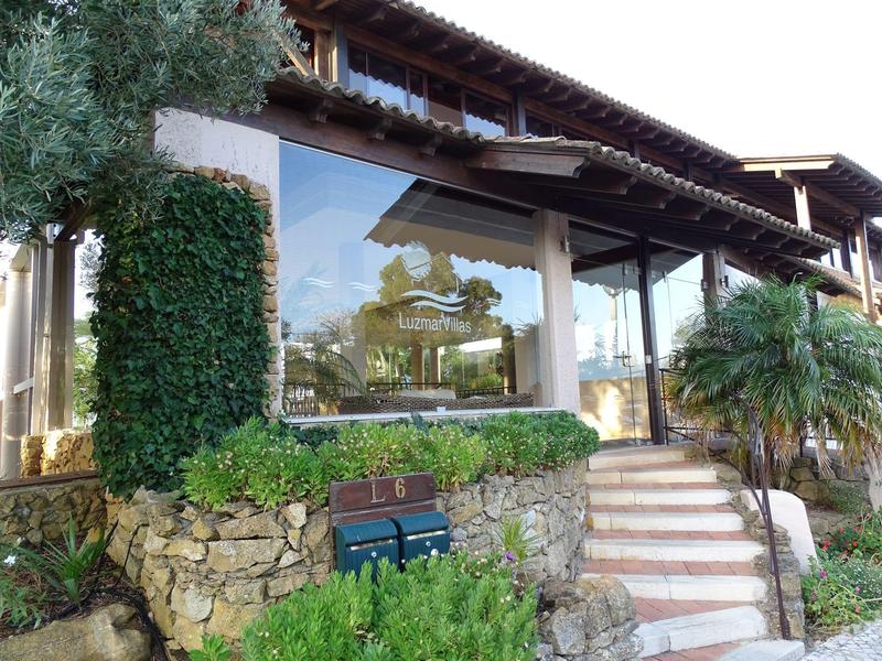 Modern hotel with large windows surrounded by green plants and a stone garden