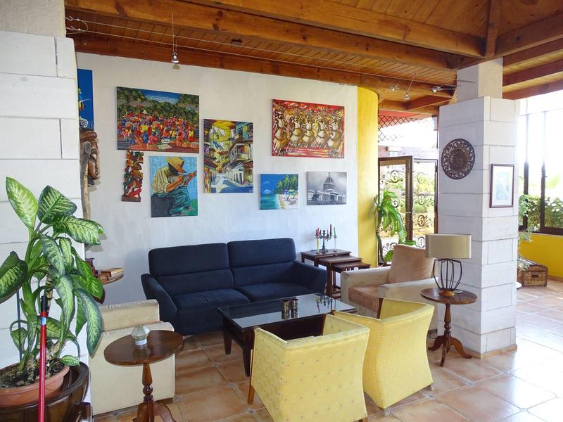 Cozy lounge area with sofa, chairs, and plants in a room with wooden ceiling.