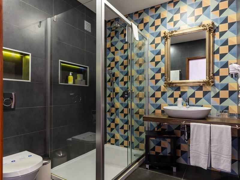 Modern bathroom with colorful geometric wall tiles, glass shower, and sink with towels.