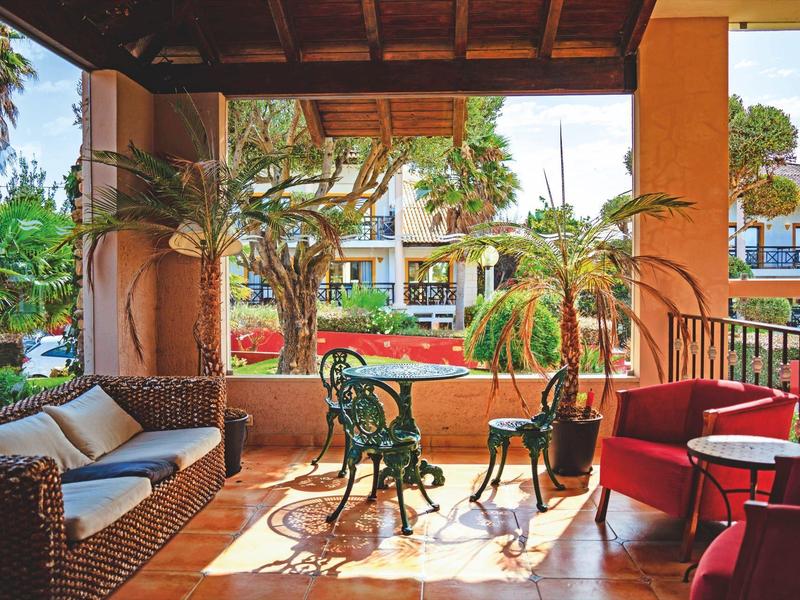 Covered terrace with cozy seating and a view of a garden with flowers and trees.