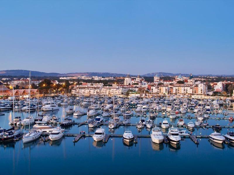Hafen mit vielen weißen Booten, ruhiges blaues Wasser, Küstenstadt und klarer Himmel im Hintergrund.