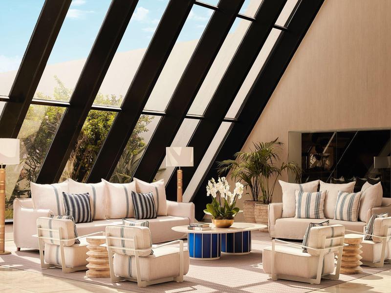 Helles Wohnzimmer mit großen Fenstern, zwei Sofas, Sesseln, Pflanzen und Couchtisch mit Dekoration.