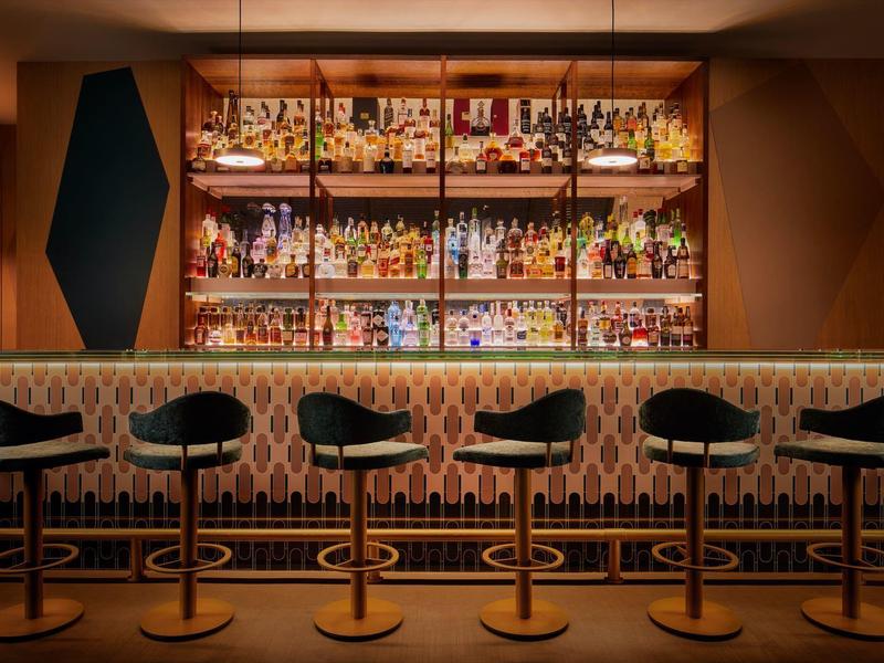 Moderne Bar mit Holzmöbeln, Sechseck-Deko und beleuchtetem Regal voller Flaschen.