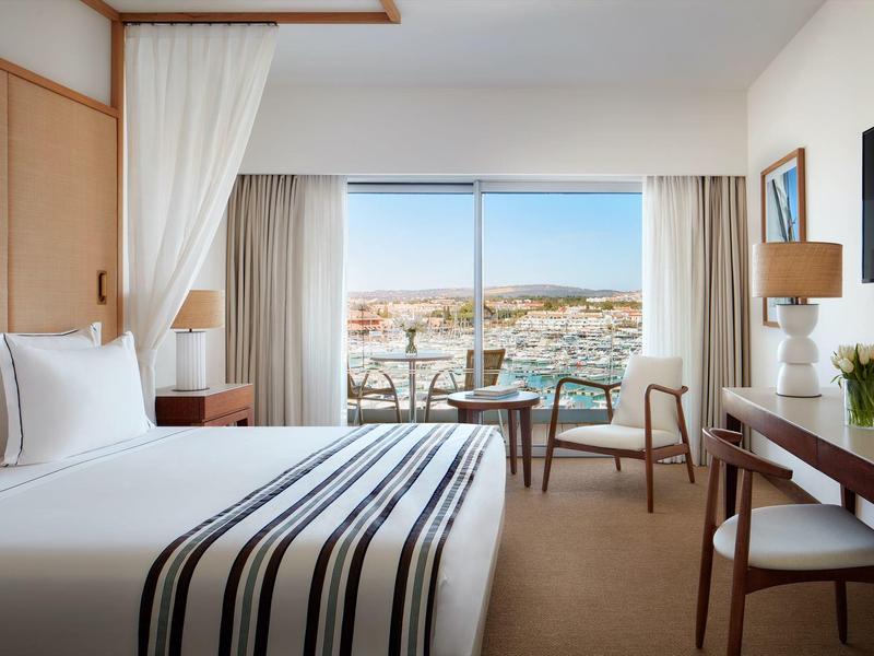 Helles Hotelzimmer mit großem Bett, Schreibtisch, Stuhl und Fenster mit Blick auf die Stadt.