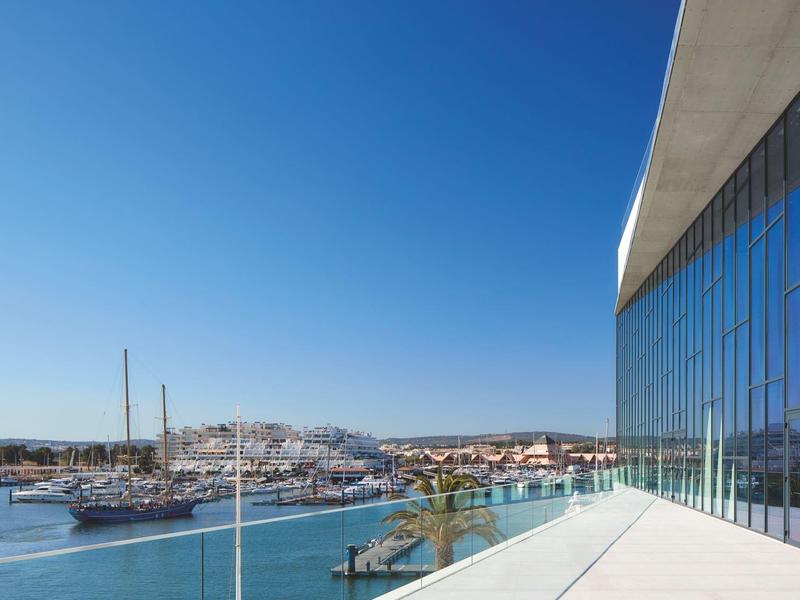 Moderner Balkon mit Glasfassade, Blick auf Hafen, Boote und klare blaue Himmelspanorama.
