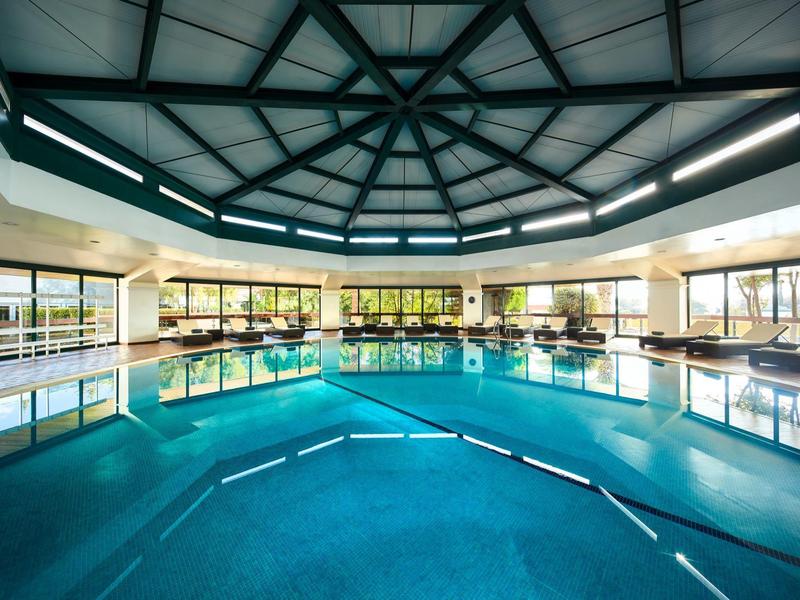 Großes rundes Hallenbad mit glattem Wasser, weißen Säulen und grauem Stahldach.