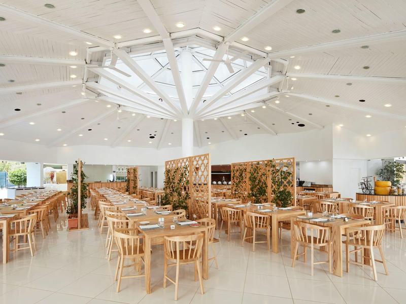 Großer, heller Speisesaal mit vielen hölzernen Tischen und Stühlen sowie rundem Deckendachfenster.