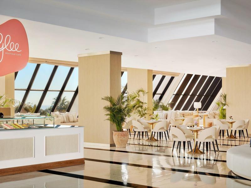 Helles Restaurant mit großen Fenstern, weißen Möbeln und gepflegten Pflanzen.