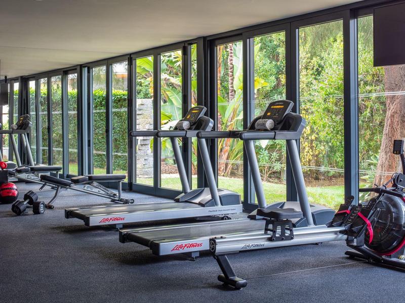 Moderne Turnhalle mit großen Fenstern und Geräten wie Laufbändern und Rudergeräten.