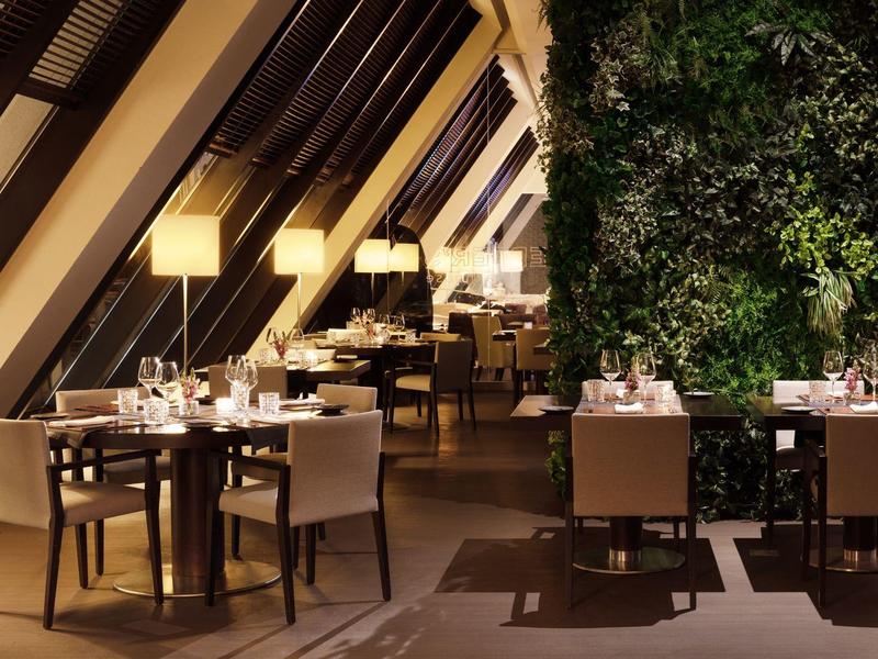 Modernes Restaurant mit Holzstühlen, gedeckten Tischen und einer großen grünen Pflanzenwand.