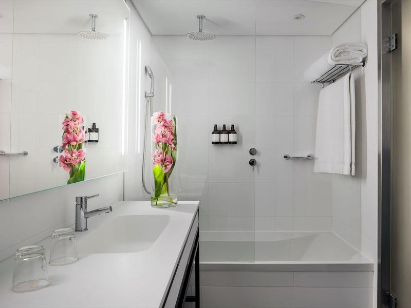 Modernes Badezimmer mit weißem Waschbecken, großem Spiegel und Duschbereich mit Glaswand und Blumen.