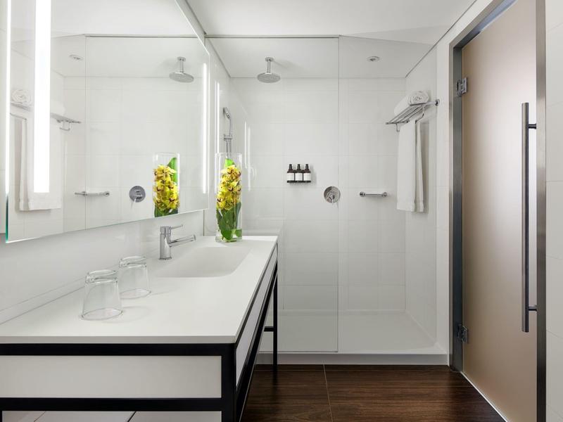 Modernes Bad mit heller Wand, großer Spiegel, weißer Waschtisch und Glasdusche mit Brausekopf.