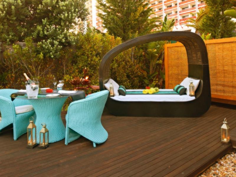 Moderner Garten mit blauem Lounge-Set und eckigem Whirlpool auf dunklem Holzdeck unter Bäumen.