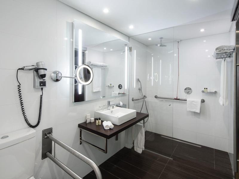 Barrierefreies Badezimmer mit großer Spiegelwand, braunem Boden und modernen Armaturen.