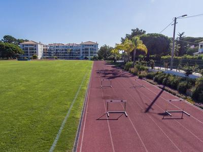 Pista di atletica accanto a un grande campo da calcio verde con edifici sullo sfondo in una giornata soleggiata.