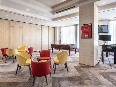 Sala luminosa con poltrone colorate, tavolo da biliardo e pianoforte in un moderno hotel.