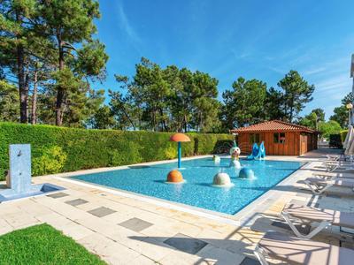 Una piscina all'aperto con varie attrazioni d'acqua e lettini vicino a un edificio dell'hotel sotto un cielo azzurro.