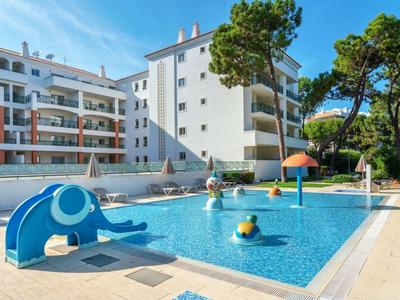 Piscina per bambini con scivolo e fungo d'acqua davanti a un edificio bianco.