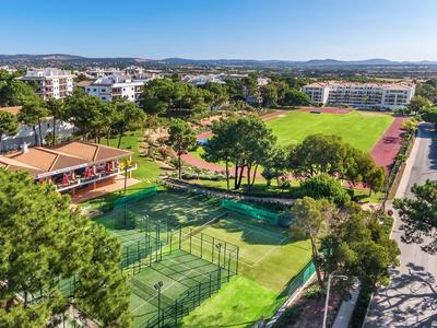 Ampio complesso alberghiero con campi da tennis, prato e vegetazione sotto cielo limpido.