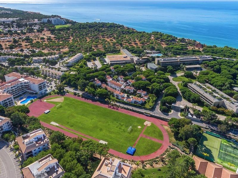 Vista aerea di una località costiera con campo sportivo, edifici e costa sullo sfondo.