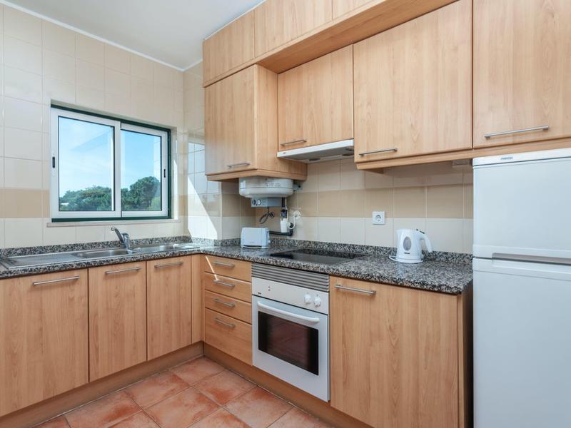 Cucina moderna con mobili in legno, piani in granito e elettrodomestici bianchi in una stanza luminosa.