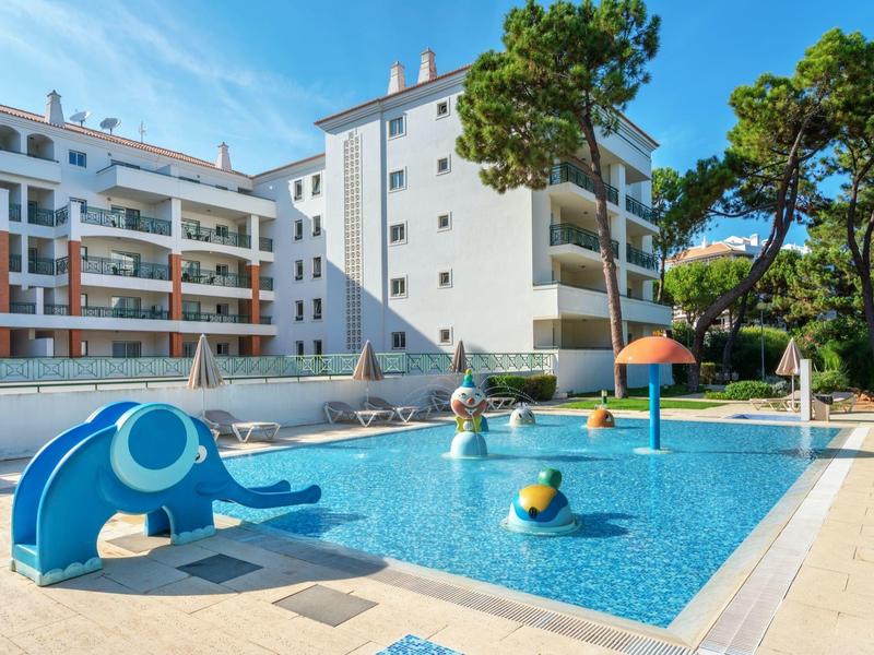 Piscina per bambini con scivolo e fungo d'acqua davanti a un edificio bianco.