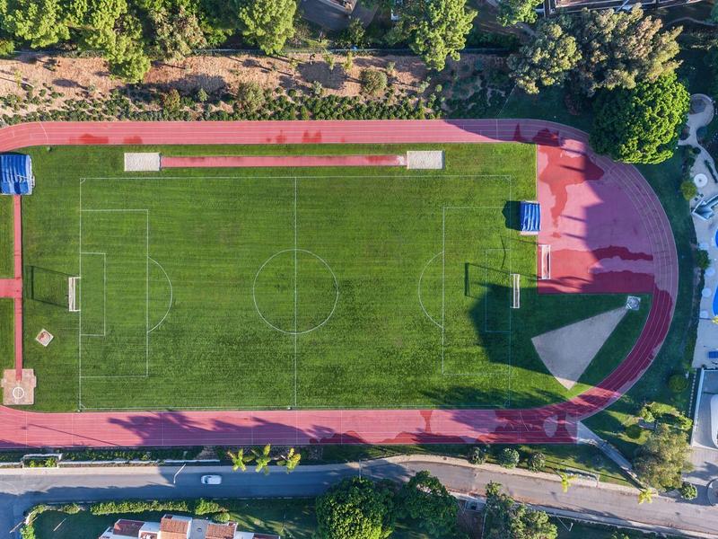 Vista aerea di un campo da calcio verde con pista di atletica e piscina vicino a un edificio.
