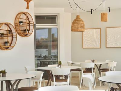 Helles Café mit weißen Tischen, Holzstühlen, runden Wandregalen und runden Lampen aus Rattan.