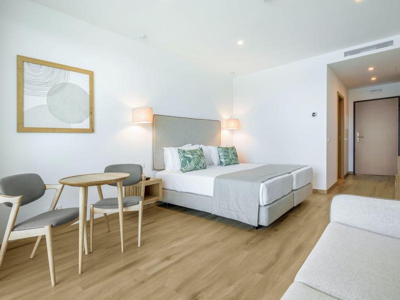 Jasny pokój hotelowy z łóżkiem podwójnym, małym stołem, krzesłami i drewnianą podłogą.