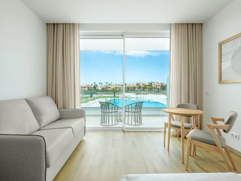 Jasny pokój hotelowy z sofą i balkonem z widokiem na morze.