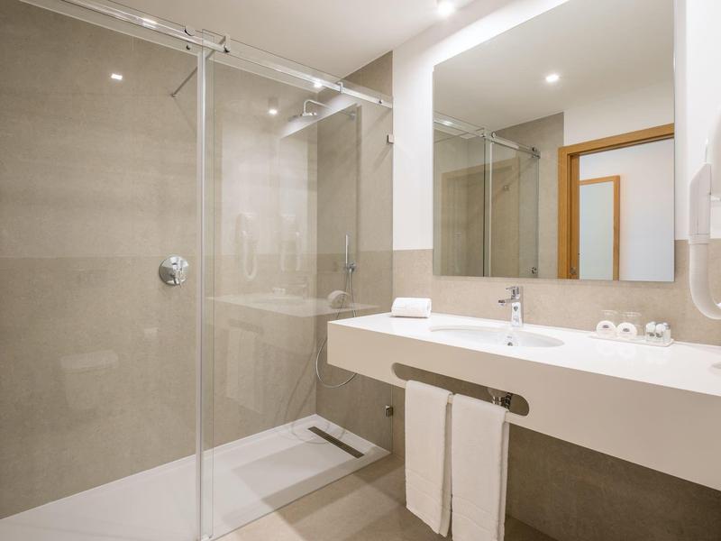 Nowoczesna łazienka hotelowa z dużym prysznicem, umywalką i oświetlonym lustrem.