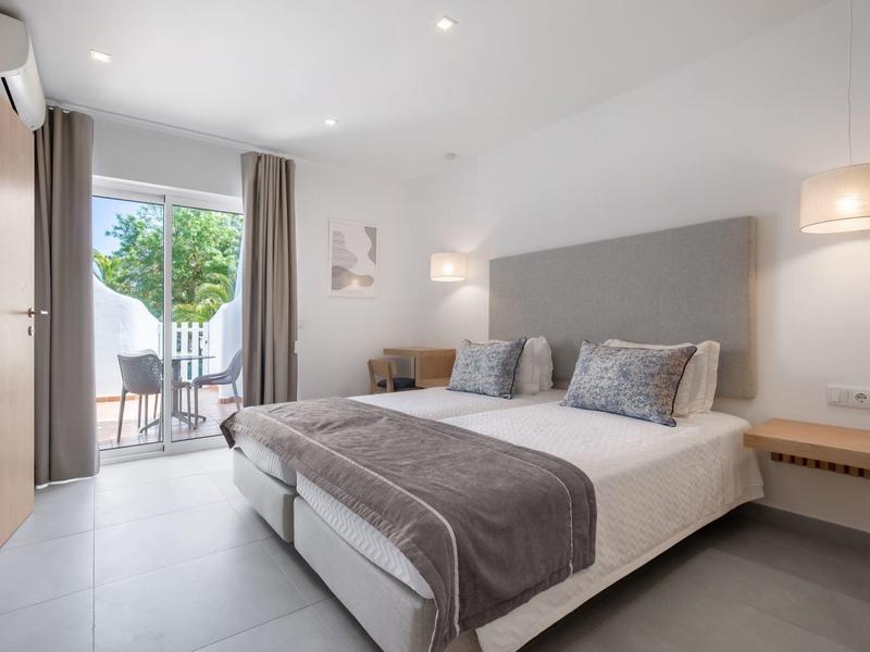 Nowoczesny pokój hotelowy z łóżkiem podwójnym, szarymi akcentami i balkonem z krzesłami.