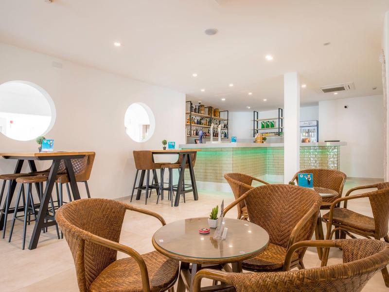 Jasna kawiarnia z okrągłymi oknami, meblami z drewna i rattanu oraz barem w tle.