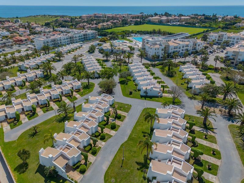 Widok z lotu ptaka na ośrodek wypoczynkowy z domkami szeregowy i zielenią, morze w tle.