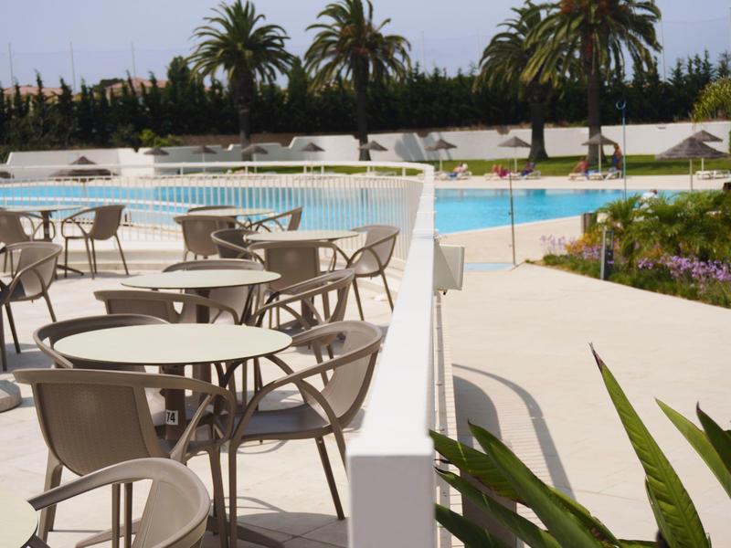 Widok na zewnętrzną przestrzeń z stołami i krzesłami obok basenu i palm