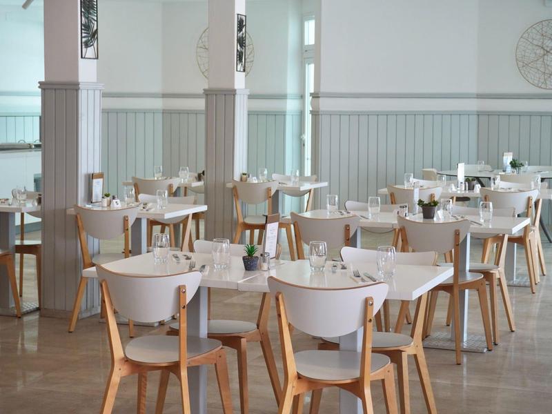 Jasna, nowoczesna jadalnia z białymi stołami i drewnianymi krzesłami w hotelu.