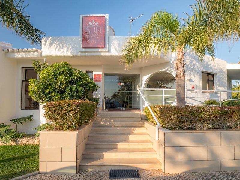 Jasny, biały budynek z schodami i palmami pod jasnym niebieskim niebem.