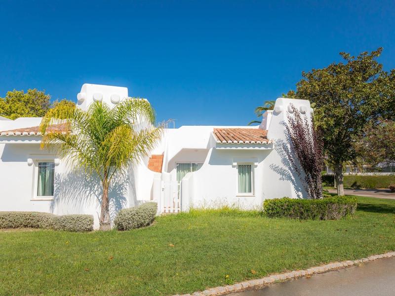 Biały domek wakacyjny z zielonym trawnikiem i niebieskim niebem w tle.