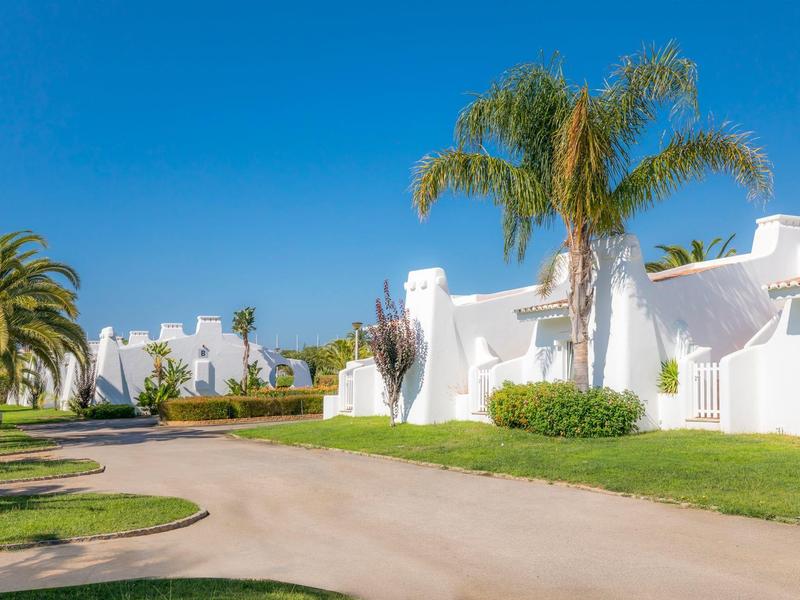 Białe budynki z łukowatymi dachami i palmami pod jasnym niebem w kompleksie hotelowym.