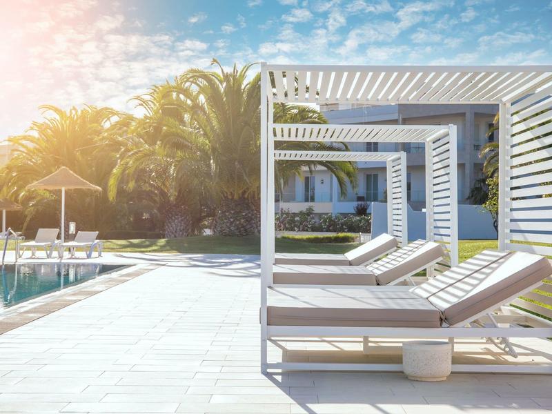 Nowoczesny basen z leżakami i pergolą w słonecznym otoczeniu hotelu.