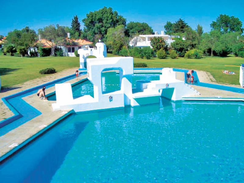 Gran piscina con agua azul y estructuras blancas modernas en un jardín verde.