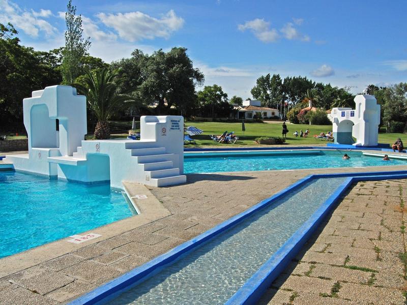 Parque recreativo con varias piscinas azules, árboles verdes y cielo parcialmente nublado.