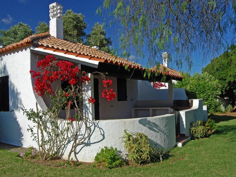 Casa de vacaciones blanca con flores rojas y jardín verde bajo cielo azul.