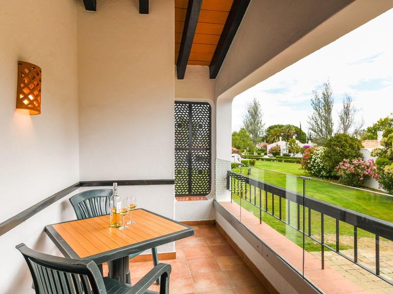 Balcón con mesa y sillas con vista a un jardín cuidado en un complejo hotelero.