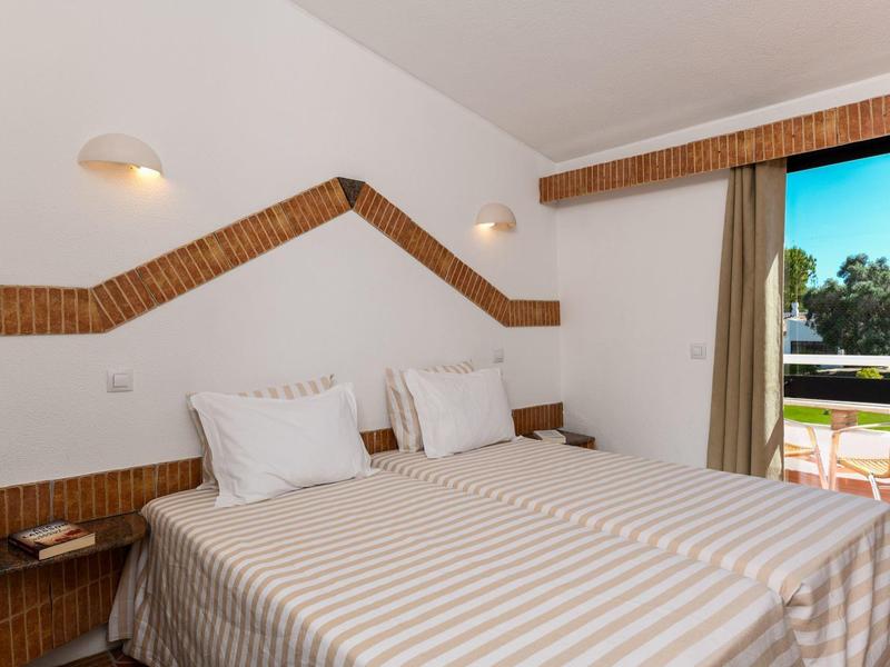 Habitación luminosa con dos camas, ropa de cama a rayas y acceso a terraza con vista al verde.