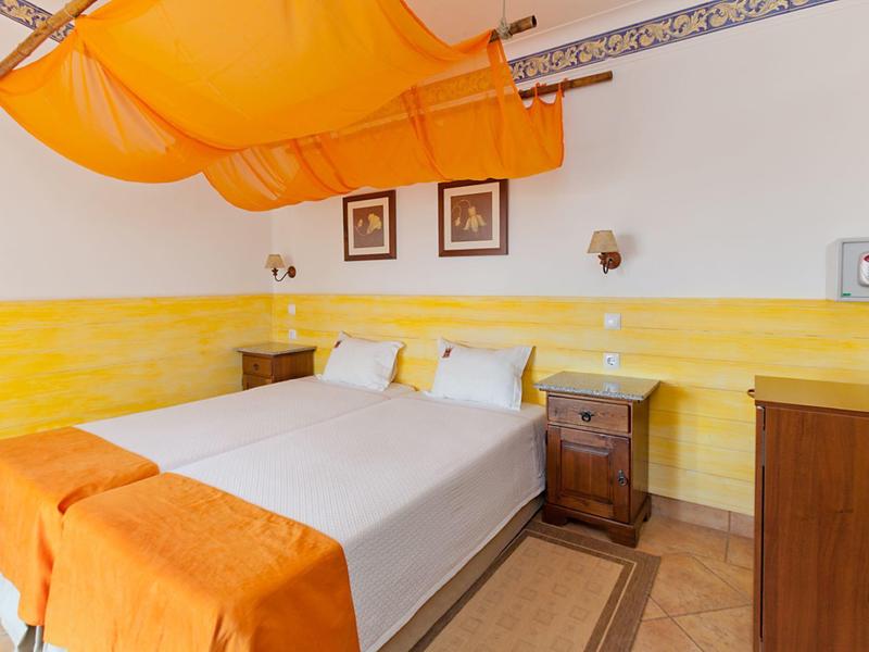 Schlafzimmer mit Doppelbett, orangefarbener Deckenverkleidung und warmen Gelb- und Orangetönen.