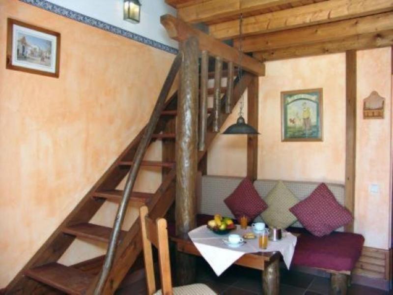 Kleines Wohnzimmer mit Holztreppe, Sitzbank, Tisch, bunten Kissen und warmen Wandfarben.